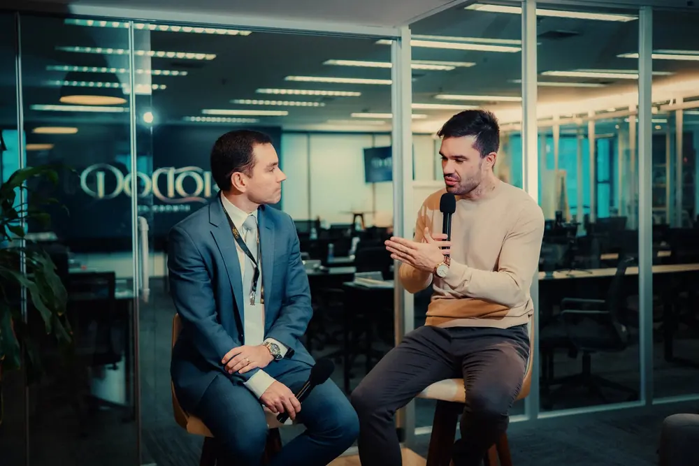 Beto Quintão entrevistando um convidado de terno azul em palco com painel do Doctor Led Growth ao fundo