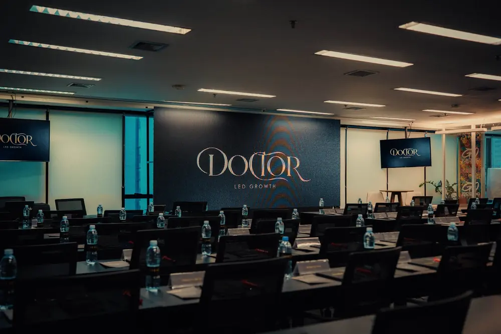 Auditório da 5G Company montado para o Doctor Led Growth, com mesas, cadeiras e painel de LED com a logomarca do evento