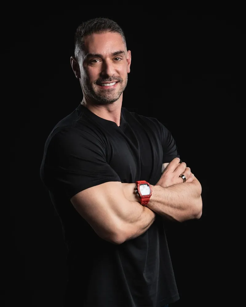 Marcelo Toledo, de camiseta preta e braços cruzados, em retrato sobre fundo preto