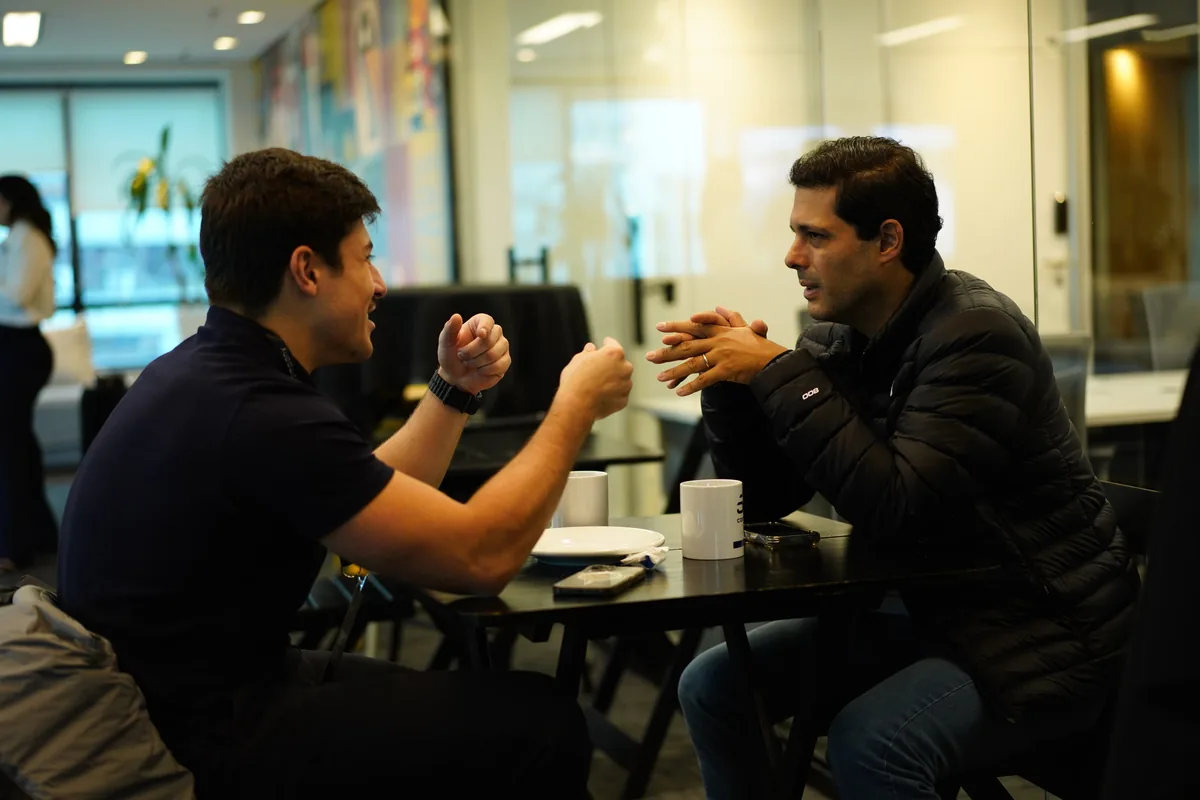 Dois membros do MedHub conversando à mesa com xícaras de café durante um encontro